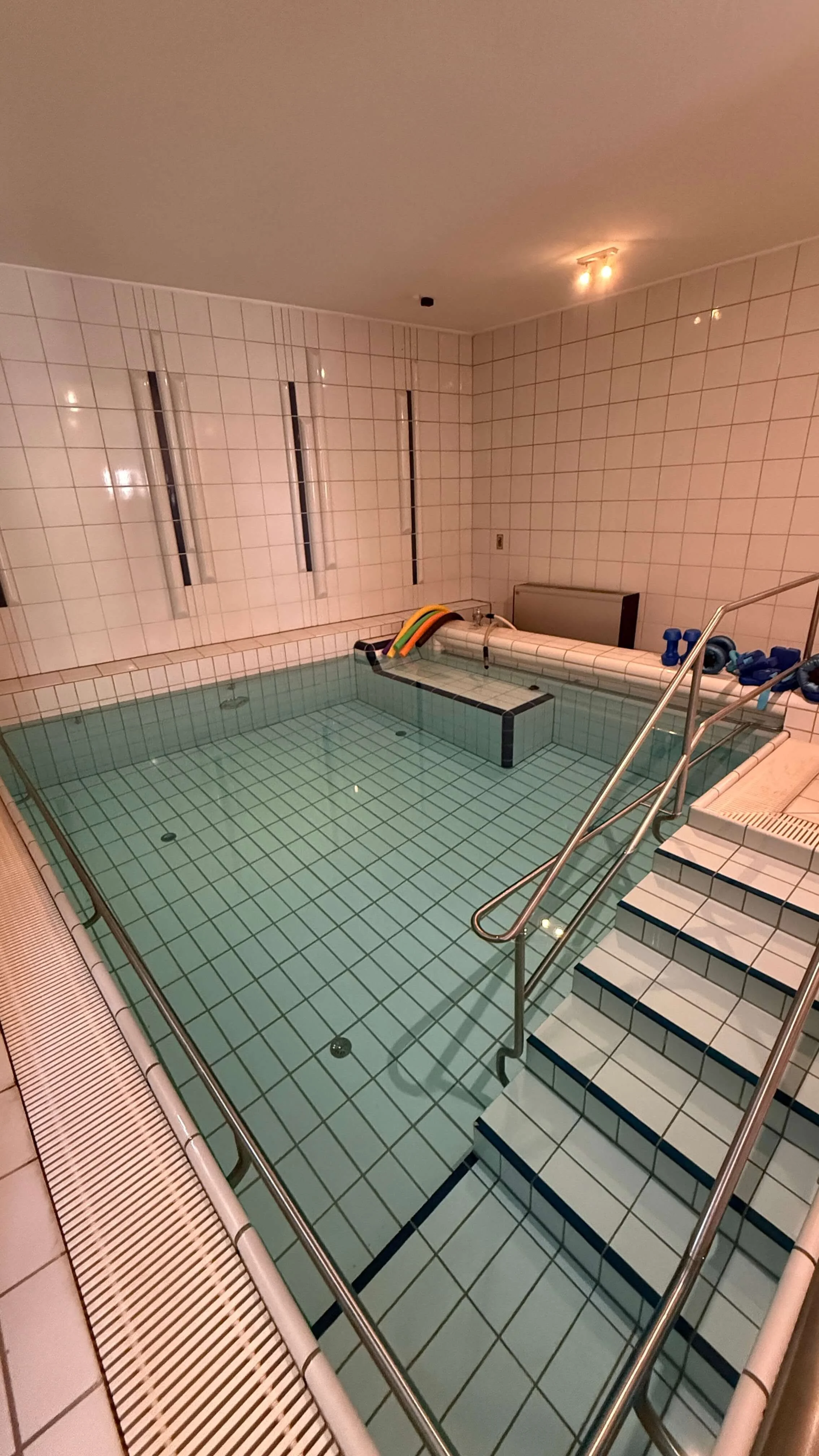 Innenaufnahme eines kleinen beheizten Schwimmbeckens mit Treppe, blauem Wasser und Wasserinspirationsmaschinen in einem Fitness- oder Wellnesscenter.